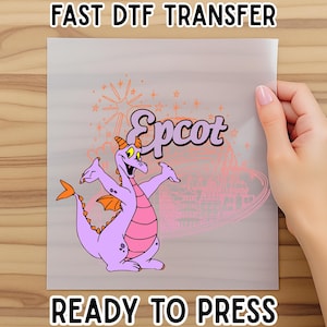 May include: A DTF transfer sheet featuring a purple cartoon dragon with orange accents and the word "Epcot" in a stylized font. The text "FAST DTF TRANSFER" and "READY TO PRESS" are also visible.
