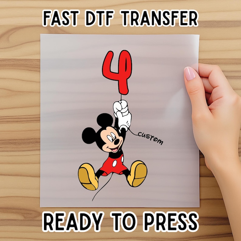 May include: A ready-to-press DTF transfer featuring Mickey Mouse holding a red number 4 balloon. The transfer includes the text "FAST DTF TRANSFER" and "READY TO PRESS". The word "custom" is written on the transfer.