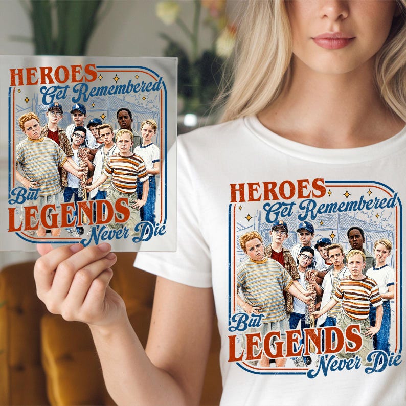 May include: White t-shirt with a graphic of a group of boys and the text "HEROES Get Remembered But LEGENDS Never Die" in red and blue. A small square print with the same design is also visible.