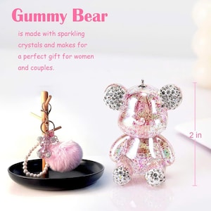 May include: A pink, sparkly Gummy Bear figurine, approximately 2 inches tall, with crystal accents on the ears, feet, and belly. The image also includes a pink pom-pom keychain and the text "Gummy Bear".