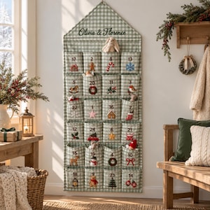 May include: A green and white gingham fabric advent calendar with a house-shaped top, featuring the embroidered text Olivia & Florence. It has twenty-four numbered pockets, each decorated with unique holiday-themed appliques and embroidery.