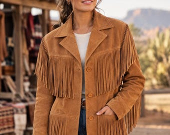 Puede incluir: Una chaqueta de ante color canela con largos flecos en el pecho, los hombros y los bolsillos. La chaqueta tiene cuello, cierre frontal de botones y mangas largas con flecos a juego a lo largo de la parte exterior de los brazos.