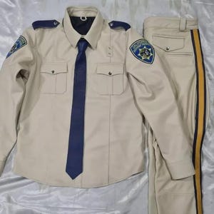 May include: A tan long-sleeve uniform shirt with a dark blue tie, two chest pockets, and California Highway Patrol patches on the shoulders, paired with matching tan trousers featuring a dark blue and yellow side stripe down the leg.