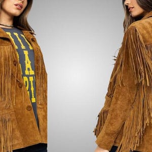 Puede incluir: Una chaqueta de ante color canela con largos flecos en el pecho, los hombros y la espalda. La chaqueta tiene un cuello clásico, cierre frontal con botones y dos bolsillos. El material de ante tiene una textura mate y un tono marrón cálido.