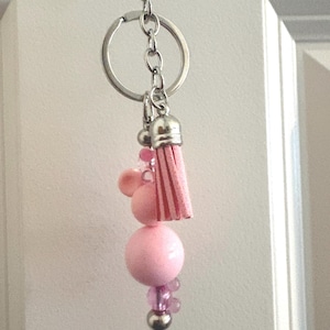 May include: Pink beaded keychain with a silver-tone clasp and chain. The keychain features a large pink bead, smaller pink beads, and a pink tassel. A small pink bead is attached to the top of the large bead.
