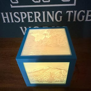 May include: A white ceramic mug with a black handle and the text "But First, Coffee" in a bold, black font. The mug is set against a blurred background, suggesting a cozy setting. The mug appears to be approximately 4 inches tall.