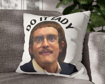 Op de afbeelding: Wit sierkussen met een man met een bril en een snor. De tekst "DO IT LADY" is in zwarte letters boven het hoofd van de man gedrukt. Het kussen ligt op een grijze bank.