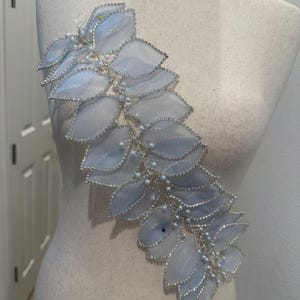 May include: A delicate, light blue leaf-shaped embellishment with silver trim and pearl accents. The leaves are arranged in a cascading pattern, creating an elegant, decorative piece. This item is likely for bridal or formal wear.