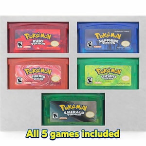 May include: A collection of five Pokemon Game Boy Advance cartridges in a gray display case. The cartridges are red, blue, red, green, and green, with the game titles visible. Text at the bottom reads "All 5 games included."