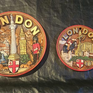 May include: Two brown, circular London souvenir plaques with raised relief details. One large plaque features Tower Bridge, Big Ben, and a guard. The smaller plaque depicts a mounted figure and a building.