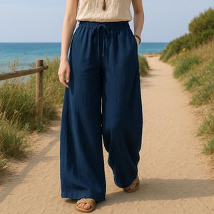 May include: Navy blue wide-leg pants with a drawstring waist. The pants are made of a lightweight fabric and have pockets. The model is wearing the pants on a sandy path near the ocean.