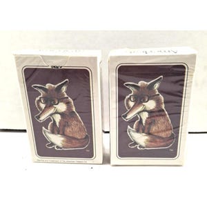 May include: Two decks of playing cards featuring a cartoon fox wearing glasses. The fox is brown and white, set against a dark brown background. The card decks are in white boxes with the text "PRO" visible.