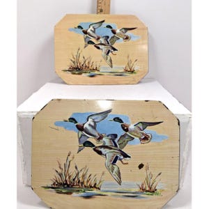 May include: Two wooden trays featuring a painted scene of ducks in flight over a pond. The trays have a light wood grain background, blue sky, and water with reeds. The ducks are in various stages of flight.