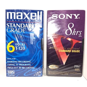 May include: Two VHS video cassette tapes. One is blue with "Maxell" and "Standard Grade" text, and the other is purple with "Sony" and "8 hrs" text. Both tapes are labeled "VHS". The Maxell tape has "6 Hours" text.