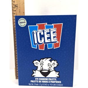 May include: A blue eye shadow palette featuring the ICEE logo in white, red, and blue. The palette includes a cartoon polar bear and the text "EYE SHADOW PALETTE" and "Net Wt./Poids: 1.2 g/0.042 oz."