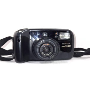 Puede incluir: Cámara negra Pentax Zoom 90-WR con lente, flash y correa negra. El logotipo de Pentax y el nombre del modelo están impresos en la parte delantera. La cámara está sobre un fondo blanco.