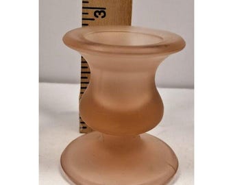 May include: A peach-colored glass candle holder with a rounded base and a flared top. The candle holder is approximately 3 inches tall. The glass has a frosted appearance. A wooden ruler is placed behind the candle holder.