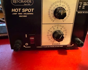 May include: Black Rio Grande Hot Spot jump ring soldering machine with a time and power dial. The machine has a red power switch and is labeled with the model number, voltage, amps, Hz, and phase. The machine is made in the USA.