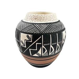 May include: A rounded ceramic vase featuring a textured cream-colored rim and a body decorated with black and white geometric patterns. The lower section of the vase displays a smooth terracotta-colored band above a solid black base.