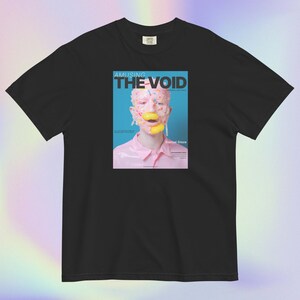 Peut inclure: Un t-shirt noir à manches courtes avec une impression graphique centrale représentant une couverture de magazine intitulée AMUSING THE VOID. L'image montre une personne couverte de glaçage rose et de vermicelles avec des bonbons jaunes.