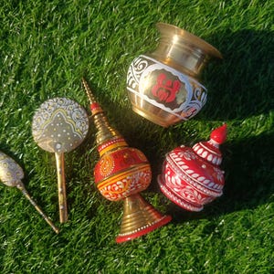 Peut inclure: Un ensemble de quatre objets décoratifs comprenant un pot en laiton avec des détails peints en rouge et blanc, un fleuron pointu peint en rouge et or, un récipient rouge à couvercle avec des motifs floraux blancs et un petit miroir à main en laiton.