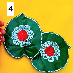 May include: Two leaf-shaped decorative items. The leaves are dark green with white dotted edges. Each leaf has a red center with white swirl designs. The background is yellow, and the number 4 is in the upper left corner.