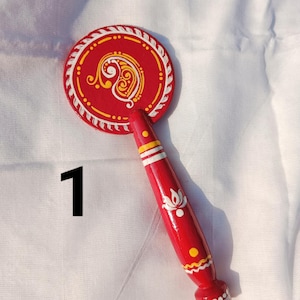 May include: A red, hand-painted wooden fan with a circular top and a handle. The top features a white and yellow paisley design on a red background, with a white border. The handle is red with white and yellow accents. The number "1" is in black.