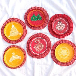 Könnte beinhalten: Eine Sammlung von sechs runden Untersetzern mit aufwendigen Designs. Jeder Untersetzer hat ein zentrales Design in Gelb oder Rot, umgeben von einem rot-rosa gemusterten Rand. Die Designs umfassen florale Muster und andere dekorative Motive.
