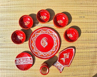 Op de afbeelding: Een set rood keramieken servies met handgeschilderde witte en oranje patronen. De collectie bevat vijf kleine kommen, één groot rond bord, één klein rond bord, een vissenvormige schaal en een klein kopje, allemaal voorzien van bloemmotieven.