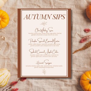 May include: A menu titled "Autumn Sips" with four cocktail recipes: Chai Whiskey Sour, Pumpkin Spiced Espresso Martini, Spiked Caramel Apple Cider, and Harvest Sangria. The menu is on a brown background with fall-themed decorations.