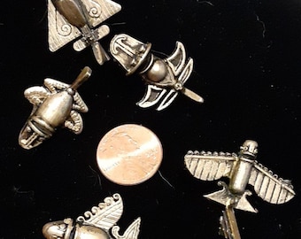May include: Five antique silver-toned metal airplane-shaped pins with intricate details, including wings and propellers. A US quarter is included for size comparison. The pins are displayed on a black surface.