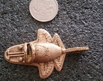 May include: A small, gold-colored, 3D printed model of a futuristic aircraft. The model has a detailed design with intricate lines and curves.