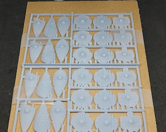 May include: A sprue of 30 grey plastic shields for miniature figures. The shields are in various shapes and sizes, and are arranged in rows on a brown cardboard backing.  30 pieces total. Sprue colors may vary. Reaper minis not included.