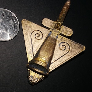 May include: A gold-colored metal pendant shaped like a triangle with a stylized bird design. The bird has a long, thin body and a small head. The pendant is about the size of a quarter.