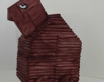 May include: A wooden toy in the shape of a red-brown ram with wheels. The toy is made of stacked wooden slats and has a single eye painted on the side.