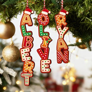May include: Christmas ornaments spelling out the names "ALBERT", "OLIVIA", and "RYAN". Each letter is a different color and design, with a Santa hat on top. The ornaments hang from red and white striped string.