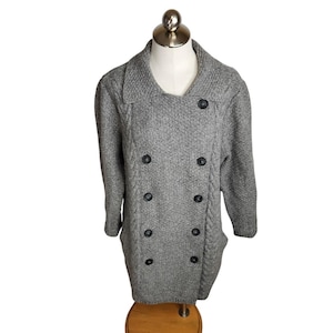 May include: A gray, double-breasted sweater coat with black buttons. The coat has a textured knit pattern and a wide collar. The sleeves are three-quarter length. The coat is displayed on a mannequin.