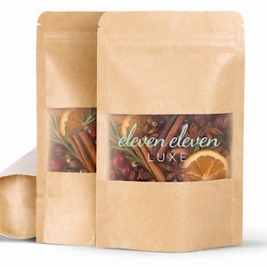May include: Two brown paper bags with clear windows displaying a mix of dried fruit, spices, and herbs. The bags have the text "eleven eleven LUXE" in teal script. Ingredients include cinnamon sticks, star anise, and orange slices.