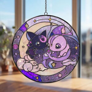 Puede incluir: Vidriera redonda que representa dos criaturas de dibujos animados en tonos morados, lavanda y negro. El diseño incluye una luna creciente, estrellas y nubes, todo sobre un fondo similar a una galaxia. La ventana está enmarcada en negro y cuelga de una cadena.