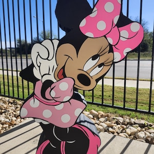 Pu&ograve; includere: Sagoma di legno di Minnie Mouse, con corpo nero, fiocco rosa a pois bianchi e gonna abbinata. Il viso del personaggio &egrave; color carne con occhi neri e lingua rossa. La sagoma &egrave; tenuta da una corda.
