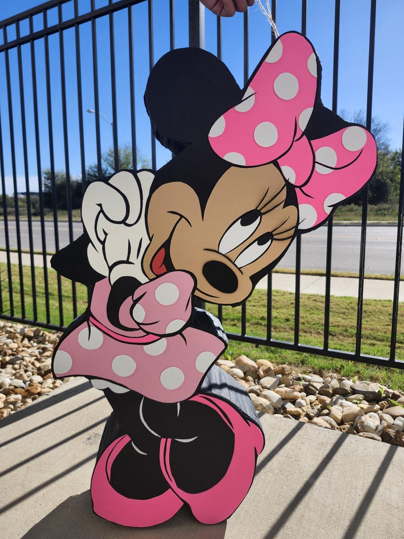 Pu&ograve; includere: Sagoma di legno di Minnie Mouse, con corpo nero, fiocco rosa a pois bianchi e gonna abbinata. Il viso del personaggio &egrave; color carne con occhi neri e lingua rossa. La sagoma &egrave; tenuta da una corda.