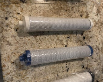 May include: Four water filter cartridges in clear plastic packaging. The top filter is yellow with black and white accents. The other three filters are cylindrical, with white or gray filter material and blue or black end caps. The filters are on a speckled countertop.