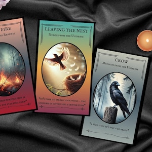May include: Three oracle cards with nature-themed illustrations and text, including "Forest Fire," "Leaving the Nest," and "Crow." The image also features lit candles, crystals, and a dark, textured background.