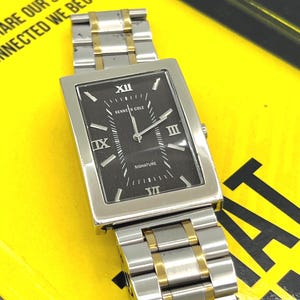 May include: A rectangular Kenneth Cole Signature watch with a black dial, silver-tone hands, and Roman numeral markers at the twelve, three, six, and nine o'clock positions. The watch features a two-tone silver and gold-colored metal link bracelet.