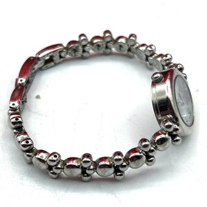 Op de afbeelding: Zilverkleurig armbandhorloge met een ronde wijzerplaat. De horlogeband heeft een reeks kleine, afgeronde en langwerpige schakels. De wijzerplaat heeft een lichte achtergrond met donkere wijzers en markeringen.