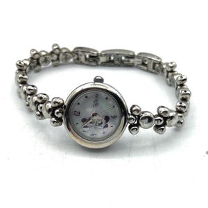 Op de afbeelding: Zilverkleurig Disney-horloge met een ronde wijzerplaat met Mickey Mouse. Het horloge heeft een band in kralenarmbandstijl. De wijzerplaat heeft een parelmoer achtergrond met zilveren wijzers en cijfers. Een klassiek Disney-thema-accessoire.