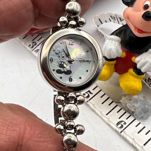 Op de afbeelding: Zilverkleurig Disney-horloge met een Mickey Mouse-afbeelding op een parelmoeren wijzerplaat. Het horloge heeft een kralenband en een ronde wijzerplaat. Een verzamelobject.