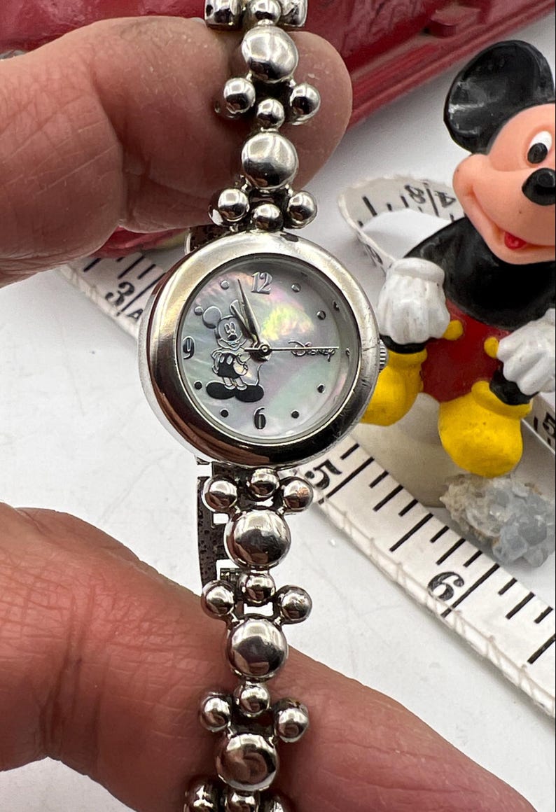 Op de afbeelding: Zilverkleurig Disney-horloge met een Mickey Mouse-afbeelding op een parelmoeren wijzerplaat. Het horloge heeft een kralenband en een ronde wijzerplaat. Een verzamelobject.