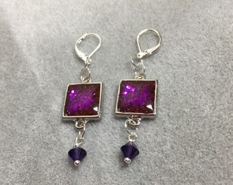 May include: A pair of silver earrings with square-shaped purple glitter resin and a dangling purple crystal.