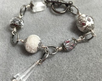 May include: A silver bracelet with clear and white beads, including a crystal-like pendant. The bracelet has a silver toggle clasp.